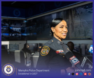 Chief Davis stands indoors in front of a room filled with multiple computer monitors and large wall screens displaying surveillance footage. Several microphones labeled with news station logos, including FOX 13 and another local channel, are positioned in front of the representative, indicating a press interview. The lower portion of the image features the Memphis Police Department emblem on the left, the text “Memphis Police Department – Established in 1827,” and the website “joinmpd.com” along with social media icons on the right, all within a blue border.