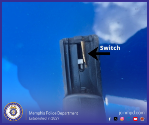 The image shows a close‑up of the rear slide area of a handgun, pointed upward against a bright blue background. An arrow labeled “Switch” points to a small metallic component installed on the back of the firearm’s slide. At the bottom of the image is the Memphis Police Department seal along with text reading “Memphis Police Department — Established in 1827” and “joinmpd.com,” accompanied by several social media icons.