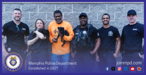The image shows a group of six individuals standing in a row in front of a light‑colored brick wall. Two small black puppies are being held by two of the individuals—one puppy is cradled in the arms of a person wearing a dark shirt on the left side of the image, and the other puppy is being held by a person wearing an orange long‑sleeved shirt near the center. Several of the individuals are wearing clothing marked with “POLICE,” and some are wearing tactical gear. At the bottom of the image is the Memphis Police Department seal, the text “Memphis Police Department — Established in 1827,” and the website joinmpd.com with several social media icons.
