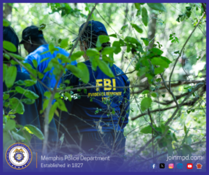 Several individuals are standing in a wooded area surrounded by dense green foliage and branches. One person in the foreground is wearing a dark blue shirt with bright yellow text on the back that reads “FBI Evidence Response Team.” More people in blue clothing are visible nearby, partially obscured by leaves. The setting appears to be an outdoor search or investigative activity. At the bottom of the image, text reads “Memphis Police Department – Established in 1827,” along with social media icons and the website joinmpd.com.