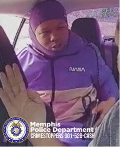 The image appears to be from an interior vehicle camera showing a person seated in a rear passenger seat. The individual is wearing a hooded jacket in shades of purple and lavender with the word “NASA” printed on the upper chest area. The person is holding an object in one hand, and the other hand is positioned near the seat. The interior of the vehicle, including the front passenger seat and part of the dashboard area, is visible. A raised hand from another individual in the front seat is also seen in the left foreground. Outside the car window, vegetation and outdoor light are visible. At the bottom of the image is the Memphis Police Department seal along with text that reads “Memphis Police Department CRIMESTOPPERS 901‑528‑CASH.”
