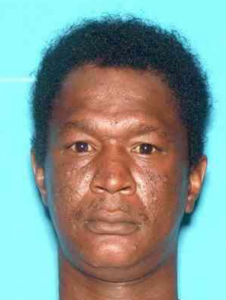 A person is shown in a portrait-style image against a solid light-blue background. The individual has short, tightly curled hair and only the neck and ears are clearly visible.