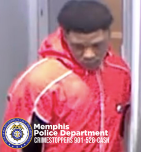 A person wearing a bright red hooded jacket with white accents stands in a narrow hallway or corridor. The jacket has a textured pattern, and the individual is seen from the upper body, facing slightly to the side. In the bottom-left corner, the Memphis Police Department badge and text read: “Memphis Police Department CRIMESTOPPERS 901-528-CASH.”