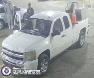 A white pickup truck with an extended cab is parked at a gas station or similar outdoor location at night. The truck has a metal utility box in the bed, along with an orange traffic cone placed on top. Several people are standing near other vehicles in the background. The ground is illuminated by overhead lighting. A logo in the bottom-left corner reads “Memphis Police Department Crimestoppers 901-528-CASH,” along with an official seal.