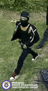 A surveillance-style outdoor image shows one individual moving across a grassy area. The individual is wearing dark clothing, including a long-sleeved top with white accents on the sleeves, dark pants, and footwear with contrasting dark and light colors. The individual also has a head covering and is carrying an item in one hand. Another individual is partially visible on the right side of the image, also dressed in dark clothing. In the lower portion, a metal outdoor chair is visible. Dense greenery fills the background. At the bottom left corner, a Memphis Police Department badge graphic appears along with text reading “Memphis Police Department CRIMESTOPPERS 901‑528‑CASH.”