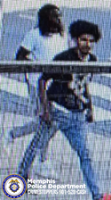 A surveillance-style outdoor image shows two individuals walking across a paved area marked with painted stripes. The individual in the foreground is wearing a dark short-sleeved top with a graphic design on the front, light-colored jeans, and footwear with dark and light contrasting colors. The individual behind is wearing a light-colored shirt and dark pants. A metal railing is visible across the lower portion of the image. In the bottom left corner, a Memphis Police Department badge graphic appears alongside text that reads “Memphis Police Department CRIMESTOPPERS 901‑528‑CASH.”