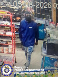 A surveillance camera image shows a person walking inside a convenience store. The person is wearing a long‑sleeved blue top and light‑colored pants with a patchwork or distressed design. The individual is walking down an aisle with shelves of packaged goods on the left and various items, including produce or bagged goods, on the right. At the bottom of the image is a Memphis Police Department badge and the text “Memphis Police Department CRIMESTOPPERS 901‑528‑CASH.” The timestamp “05‑08‑2026” is displayed at the top of the image.
