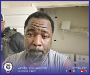 A person in a gray sleeveless shirt stands indoors in what looks like a laundry area, with washing machines and shelves behind them. Another individual in dark tactical gear is partially visible in the background. A border around the image includes Memphis Police Department branding, its seal, and the website “joinmpd.com” with social media icons.