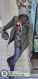 A surveillance‑style image taken inside what appears to be a retail or convenience store. The person in the image is wearing a hooded jacket with the hood up, a layered shirt underneath, jeans with a faded or worn pattern, and dark footwear. The person is holding an object in one hand while walking along a tiled floor near a checkout or service counter. On the lower left corner of the image, there is a Memphis Police Department emblem along with text that reads “Memphis Police Department CRIMESTOPPERS 901‑528‑CASH.” Shelving, merchandise displays, and store fixtures are visible in the background.