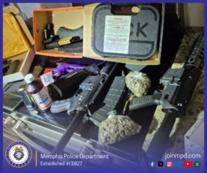“An assortment of items displayed on a countertop, including multiple firearm components and magazines, two clear plastic bags containing plant material, several open boxes with packing materials, and a dark-colored hard gun case labeled with large printed text. A bottle with a white cap and a printed label sits near the front of the arrangement. The lighting is bright and focused on the items. At the bottom of the image, a blue gradient banner includes a circular badge-like graphic and the text ‘Memphis Police Department – Established in 1827,’ along with the website ‘joinmpd.com’ and several social media icons.”