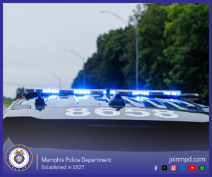 The roof of a Memphis Police Department vehicle is shown with bright blue emergency lights illuminated. Large white numbers are visible on the top of the vehicle. The scene is outdoors along a roadway bordered by trees, with streetlights lining the road. At the bottom of the image, the Memphis Police Department seal appears alongside the text “Memphis Police Department – Established in 1827,” the website joinmpd.com, and several social media icons.