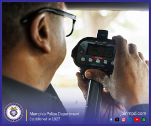 A Memphis Police Department officer holds and operates a handheld police lidar speed‑measuring device inside a vehicle. The display on the device shows numerical readings. The background outside the window is bright and slightly out of focus. At the bottom of the image, the Memphis Police Department seal is shown along with the text “Memphis Police Department – Established in 1827,” the website joinmpd.com, and several social media icons.