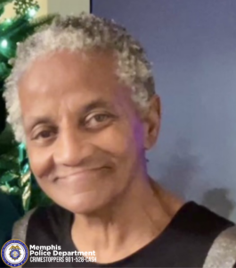 An older person with short, curly gray hair is shown indoors, wearing a dark top. Behind them is a decorated Christmas tree with lights and ornaments, set against a blue wall. In the lower-left corner, there is a Memphis Police Department Crimestoppers logo with the text “901‑528‑CASH.”