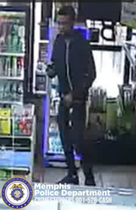 A surveillance-style photo shows a person standing inside a convenience store. They are dressed in dark clothing and holding an object in one hand. Behind them are shelves stocked with drinks and other items. At the bottom of the image is a Memphis Police Department Crimestoppers banner with the phone number 901‑528‑CASH.