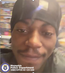 A person wearing a dark hooded garment stands indoors, facing slightly to the side. Their face is mostly in shadow. Behind them are shelves stocked with assorted items, suggesting a store or similar retail environment. In the lower-left corner, a Memphis Police Department CrimeStoppers badge and the text “901‑528‑CASH” appear.