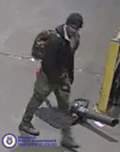 A person wearing a dark jacket, camouflage-style pants, and boots is walking on a paved surface while carrying a large leaf blower. A patterned backpack is worn over one shoulder. A yellow post is visible to the right, and the Memphis Police Department seal and CrimeStoppers contact information appear in the bottom-left corner.