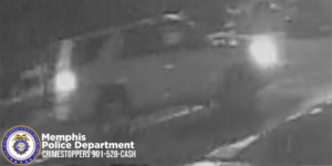A grainy, black‑and‑white surveillance image shows a large SUV traveling on a roadway at night. The vehicle’s headlights and taillights create bright glare in the low‑quality footage, obscuring many details of the vehicle. The SUV appears to be moving from left to right. In the lower-left corner, a Memphis Police Department seal is visible along with text that reads “Memphis Police Department CRIMESTOPPERS 901‑528‑CASH.