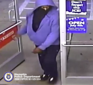 A person wearing a hooded sweatshirt with the hood pulled up and a cloth covering the lower portion of the head is entering a store through a glass door. The person is wearing a light-colored hoodie, dark pants, and dark shoes with lighter markings on them. The scene appears to be from a security camera inside a store. On the right side of the door, several signs are visible, including one that reads “Don’t forget the ICE!” and another advertising that the store is open on July 4th. At the bottom-left corner of the image, a Memphis Police Department badge logo is present along with the text “Memphis Police Department CRIMESTOPPERS 901-528-CASH.”