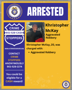 A public information graphic with a blue and yellow design featuring the Memphis Police Department seal at the top. Large white text across a blue banner reads “ARRESTED.” Below, on the right side, there is a photo of an unidentified adult seated inside what appears to be the back seat of a police vehicle. Beside the photo, black text states: “Khristopher McKay — Aggravated Robbery.” Further text below says: “Khristopher McKay, 20, was charged with: • Aggravated Robbery.” On the left side of the graphic, there is a blue shield-shaped Crime Stoppers logo with white text: “Crime Stoppers — 901‑528‑CASH.” Additional text below reads: “www.crimestopmem.org. Contact Crime Stoppers anonymously 901‑528‑2274. You could be eligible for a cash reward!” A small Memphis Police Department seal is in the bottom-right corner.