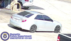 A surveillance-style image shows a red midsize SUV parked or moving slowly on a concrete surface in an outdoor area. The vehicle has a shiny finish, chrome accents, tinted windows, and a sunroof. The SUV is viewed from the side at a slight angle, showing all four wheels and the full length of the vehicle. In the lower-left corner of the image, the Memphis Police Department Crime Stoppers logo and contact information are visible. Other vehicles can be seen partially in the background.