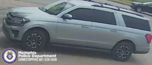 A surveillance-style image shows a silver SUV parked or moving on a paved surface. The vehicle has dark-tinted windows, black wheels with a multi-spoke design, roof rails, and a front grille with chrome accents. Another vehicle is partially visible in the background on the right side. In the lower left corner, there is a Memphis Police Department badge logo along with text that reads: “Memphis Police Department CRIMESTOPPERS 901-528-CASH.”