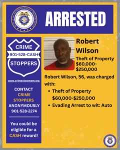 A rectangular poster with a yellow and blue background design. At the top, a wide blue banner displays the word “ARRESTED” in large white letters. On the left side of this banner is a circular seal labeled “City of Memphis Police Department.” Below, on the left side of the poster, there is a large blue shield-shaped graphic with white text that reads: “CRIME STOPPERS 901-528-CASH” Under the shield is the website “www.crimestopmem.org,” followed by additional text: “CONTACT CRIME STOPPERS ANONYMOUSLY 901-528-2274 You could be eligible for a CASH reward!” To the right of the shield is a rectangular photo showing one individual posed against a height chart background. To the right of the photo, black text reads: “Robert Wilson Theft of Property $60,000–$250,000 Robert Wilson, 56, was charged with: • Theft of Property $60,000–$250,000 • Evading Arrest to wit: Auto” In the bottom right corner of the poster, there is another small circular Memphis Police Department seal.