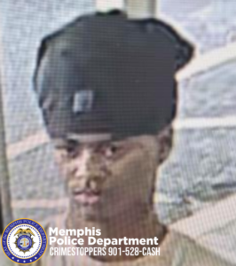 An image shows an individual standing indoors near a window or glass door. The individual is wearing a dark head covering or cap positioned loosely on the head. The person’s face is visible, looking forward. Part of a light‑colored shirt can be seen. The background includes window framing with bright outdoor light. At the bottom of the image, there is a Memphis Police Department emblem and text that reads “Memphis Police Department CRIMESTOPPERS 901‑528‑CASH.”