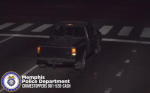 A dark-colored pickup truck is shown driving on a roadway at night. The truck is photographed from behind and slightly to the left. Its rear lights are illuminated, and it appears to be traveling through an intersection marked with white pedestrian crosswalk lines. The background is dark. In the bottom-left corner, there is a Memphis Police Department badge and text that reads: “Memphis Police Department CRIMESTOPPERS 901-528-CASH.