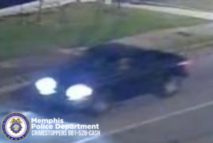A blurry nighttime surveillance image shows a dark-colored pickup truck traveling on a roadway. The truck’s headlights are brightly illuminated, creating a strong glare that obscures some front details. The vehicle appears to be moving from left to right. A grassy area and a sidewalk are visible in the background. In the bottom-left corner, a Memphis Police Department badge and the text “Memphis Police Department CRIMESTOPPERS 901-528-CASH” are displayed.