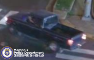 A nighttime surveillance image shows a dark-colored pickup truck traveling through an intersection. The truck is captured from an elevated angle, moving toward the right side of the frame. Its rear lights are illuminated, and the vehicle is positioned partly over white crosswalk markings. A person is visible inside the cab, though details are unclear due to image quality. A sidewalk, curb, and a utility pole are seen along the right edge of the image. In the bottom-left corner, a Memphis Police Department badge and the text “Memphis Police Department CRIMESTOPPERS 901-528-CASH” are displayed.