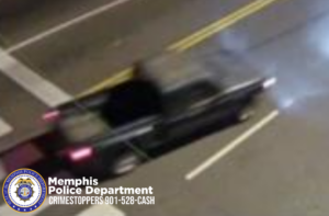 A nighttime surveillance image shows a dark-colored pickup truck traveling on a wet roadway. The truck is moving toward the right side of the frame and is slightly blurred due to motion. Its rear lights are illuminated, and steam or exhaust is visible near the front of the vehicle. The road has yellow center lines and white crosswalk markings at the bottom of the frame. In the lower-left corner, a Memphis Police Department badge and the text “Memphis Police Department CRIMESTOPPERS 901-528-CASH” are displayed.
