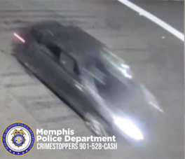 A blurry surveillance image shows a dark-colored sedan driving across a roadway at night. The vehicle appears in motion, with headlights illuminated and details obscured due to motion blur. Road markings are visible, including a white line near the top right corner. The bottom left of the image displays the Memphis Police Department CrimeStoppers logo and the text “Memphis Police Department CRIMESTOPPERS 901-528-CASH.