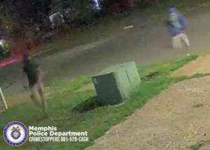 A grainy nighttime surveillance image shows two unidentified individuals running across a grassy area near a street. One individual on the left is wearing a dark top and light shorts. The other individual on the right is wearing a hooded sweatshirt and light shorts. A large green utility box is positioned in the center foreground. At the bottom left, a Memphis Police Department badge and the text “Memphis Police Department CRIMESTOPPERS 901-528-CASH” are visible.
